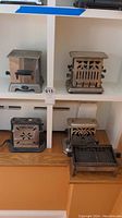 Photo shows five vintage metal toasters arranged on shelves, different shapes and vent cutout patterns visible.
