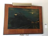 Framed wall art showing a streamlined train locomotive at night under moonlight with illuminated headlight, wood-finished frame