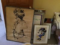 Four framed artworks leaning against wall near doorway and bed.