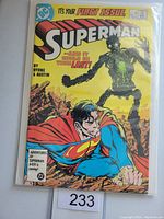 Front cover of Superman #1 comic book showing vibrant yellow cover with Superman and a green robotic figure, with issue text and the number 233 auction tag visible.