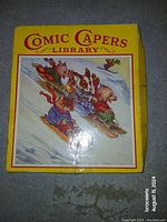 Front cover of the Comic Capers Library children's book showing four animals sledding in winter clothing on a snowy hill.