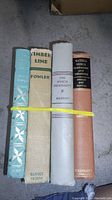 Four books standing upright bound together with yellow rubber band, titles visible on spines.