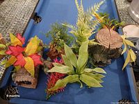 Overview of several artificial aquarium plants with colorful leaves mounted on log style bases for aquarium decoration.