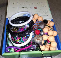 Box with assorted jewelry including plastic bangles, bead necklace, colorful bracelets, and a pin with red flower.