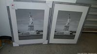 Two framed black and white photos of the Statue of Liberty leaning against a wall.