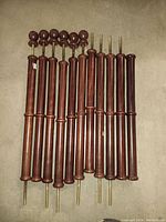 10 reddish-brown polished wooden staircase spindles laid out side by side on a concrete floor, showing overall shape and metal rods for mounting.