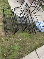 Four black metal shoe racks placed on grass outdoors, showing full view of all racks lined up side by side.