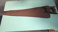 Full view of antique Spear & Jackson handsaw with rusty 30 inch blade and wooden handle.
