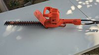Orange Black & Decker 16-inch hedge trimmer laying on white table, showing full length and blade side view.