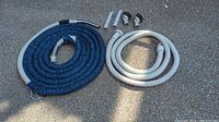 Two central vacuum hoses coiled on ground: one long blue fabric-covered hose approximately 34 feet, one shorter white plastic hose approximately 12 feet. Two straight wand attachments and two elbow hose fittings placed nearby.