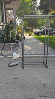 Full view of clothes steamer and metal clothing rack on wheels outside on pavement