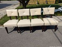 Front view of four cream leather upholstered chairs with dark wood tapered legs