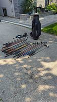 Overview photo of golf clubs laid out on pavement next to black golf bag.