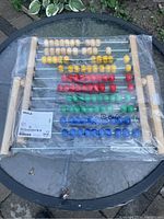 Front view of new, unopened IKEA MULA abacus showing colored beads and wooden frame under plastic wrapping.