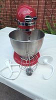 Front view of red stand mixer with bowl and three attachments laid out