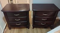 Pair of three drawer dark mahogany nightstands shown side by side, showing overall furniture shape and condition.
