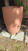 Full view of the terracotta rain barrel placed outdoors on concrete blocks, showing the front and side.