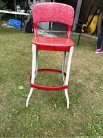 Photo showing front angle of retro red vinyl and steel stool with supportive back and curved legs on grass