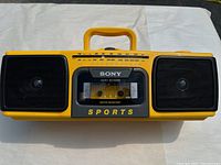 Front view of yellow Sony boombox showing cassette door, speakers, and radio tuner