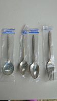 Four pieces of Wallace Sterling silver flatware: one fork, three spoons of varying sizes, each with detailed Spanish Lace pattern handles, all sealed in plastic bags.