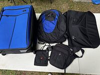 Full set of Victorinox Swiss Army luggage and travel bags including carry-on luggage, backpack, sling bag, fanny pack, and passport pouch all laid out on a white table taken outdoors on grass.