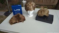 Three wigs displayed on white table, one on mannequin head, two with boxes
