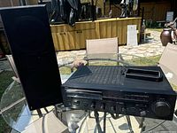 Yamaha stereo receiver and black R5 Plus speaker on glass table outdoors.