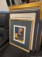 Five framed prints stacked, front frame gold finish with green mat visible