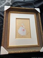 Full view of framed artwork with corner protectors showing ornate gold frame and cream mat