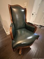 Front angled view showing the dark green leather upholstery and wood frame with brass nailhead trim on arms and sides.