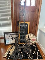 Three Eiffel Tower shaped metal wine racks in black on wooden floor with Paris themed clocks and signs behind them.