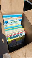 Photo of children's books inside a cardboard box showing colorful spines and titles such as 'Albert'.