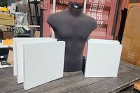Black fabric-covered hangable mannequin torso surrounded by six white metal display stands on a wooden surface.