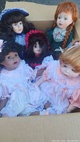 Close up of five porcelain dolls in a cardboard box, showing detailed clothing and hairstyles.