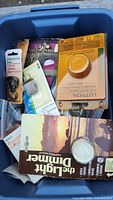 Bin with assorted electrical items including dimmer switches, wiring accessories, and face plates in packaging.