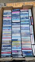 View of the box filled with cassette tapes showing a large variety of music titles and artists.