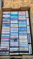 Photo showing a box filled with cassette tapes arranged in rows and columns, titles visible on tape labels