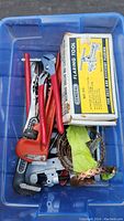 Plastic bin containing various plumbing tools with red handles, flaring tool box, pipe cutter, pipe wrench, and other hardware
