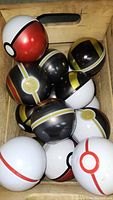 Photo showing a crate filled with twelve metal Pokémon balls of various types including Poké Balls, Ultra Balls, and Great Balls with detailed paint and logos.