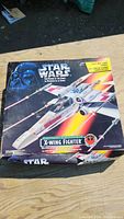 Front of the Star Wars X-Wing Fighter box showing the toy with colorful space background and Darth Vader's face in the top left.