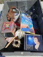 Overview of the bin contents showing CDs, VHS tape, tools, glass goblets, tin toy container, ceramic jar, and figurine
