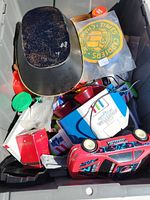 Top view of storage bin showing a red toy car, vintage painted metal trays, collectible packaging boxes, and other various items.