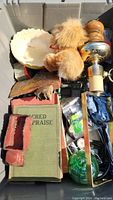 Photo showing various collectible items including a green book, teddy bear, shell dish, wooden object, and other miscellaneous items inside a storage bin.