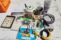 Photo showing assorted collectibles including teapot, boxed Oxo truck model, helicopters in plastic bag, toys, books, keychains, and cups spread on wooden surface.