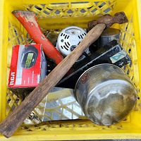 View of various hand tools including claw hammer, orange handled axe, mallet, and saw blades, plus a metal bowl and RCA clock box in a yellow crate.