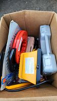 Box containing assorted tools including cable reel, yellow hand tool, and gray plastic case