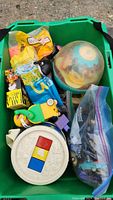 Top view of the toy bin showing a globe toy, round white musical toy, yellow duck toy, small packaged toys, and a bag of assorted figures.
