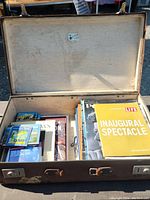Open vintage suitcase showing neatly organized contents including JFK memorabilia books, LIFE magazines, postcards, and music CDs.