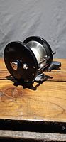 Side view of black Penn trolling reel showing spool and handle on wooden surface