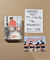 Stack of collector cards with a handwritten note indicating the complete set of 90 cards from 1966-1996, featuring a band member on the top card and a group photo card below the note.
